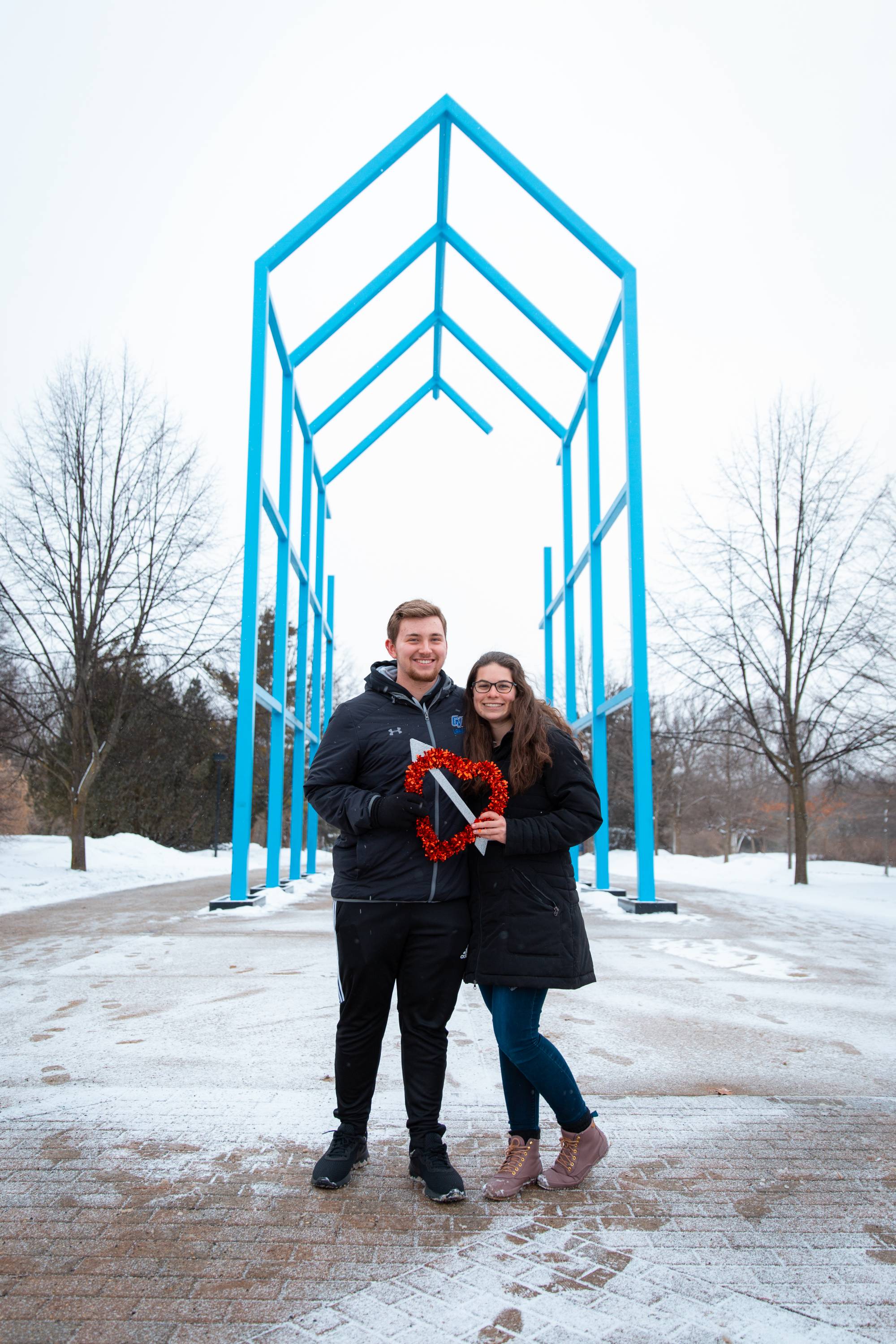 GVSU couple holding a heart in front of the blue arch